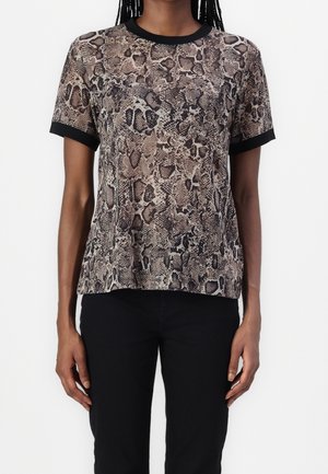 Femme portant un t-shirt à manches courtes imprimé serpent avec col et poignets noirs, associé à un pantalon noir.
