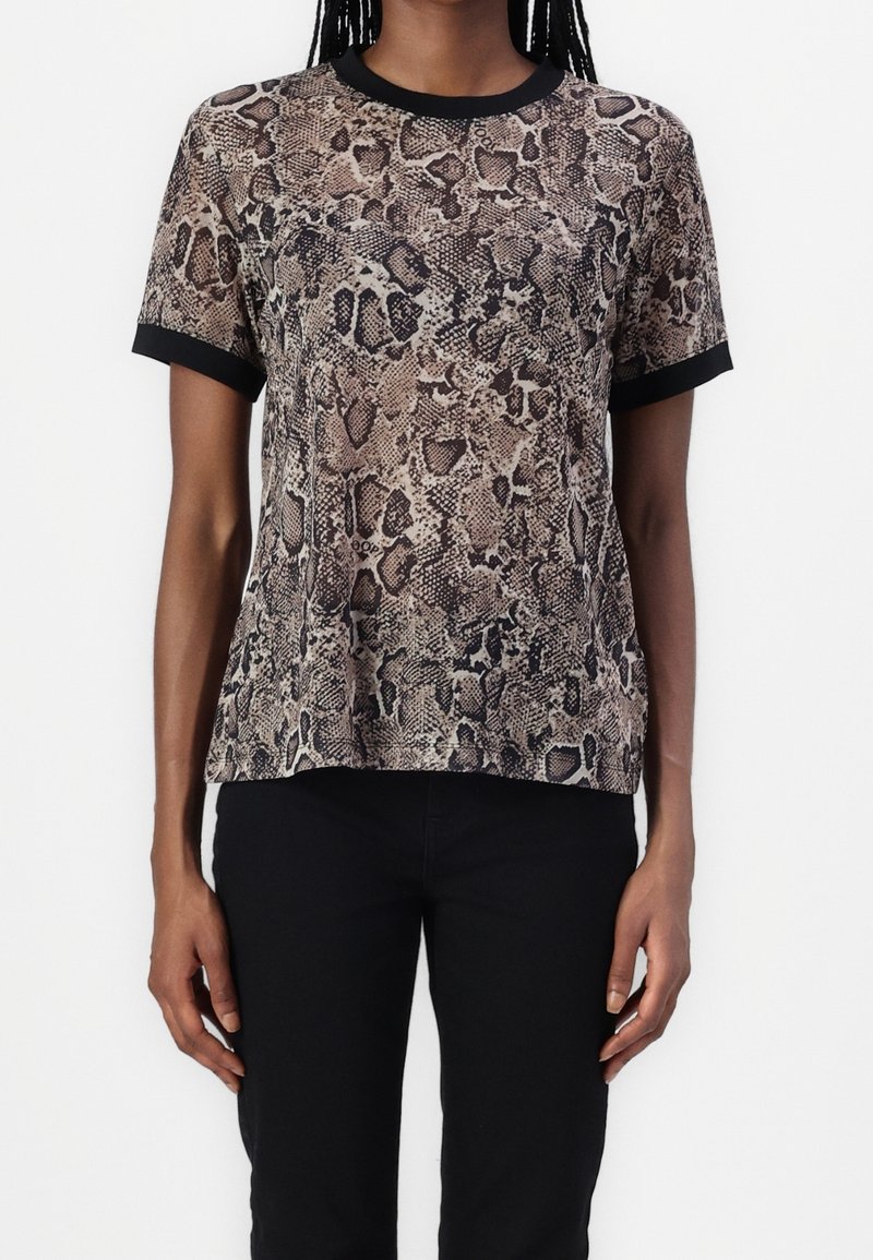 Femme portant un t-shirt à manches courtes imprimé serpent avec col et poignets noirs, associé à un pantalon noir.