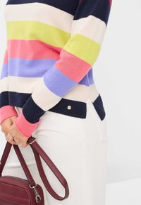 Gestreifter Pullover in Pink-, Marineblau- und Grüntönen. Hergestellt aus weichem Material, mit taillierter Form und seitlichem Schlitzdetail, kombiniert mit einer burgunderfarbenen Tasche.
