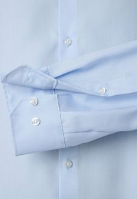 Lichtblauwe dressshirt van gestructureerde stof. Beschikt over knoopmanchetten en contrasterende witte knopen. TAILORED fit en een gladde afwerking.