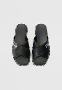 Black slide sandals with crisscross straps, made of smooth leather, featuring white embroidered logo, and stitched detailing along the edges.
