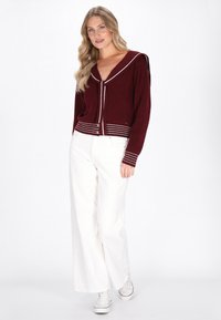 Cardigan in maglia bordeaux con colletto da marinaio e dettagli a righe bianche, abbinato a pantaloni bianchi a gamba larga e sneakers bianchi.