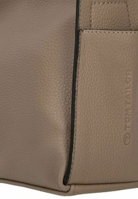 Sac à main en cuir beige avec une surface texturée, une forme arrondie, des accents noirs et un logo visible. Présente des coutures le long des bords.