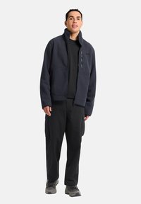 Marineblauwe geribde fleecjacket met hoge kraag, ritszak en twee zijzakken, gecombineerd met zwarte cargobroek en grijze wandelschoenen.