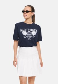 T-shirt en coton bleu marine avec impression graphique blanche de raquettes de tennis, associé à une jupe plissée blanche. Comprend un col rond et des manches courtes.