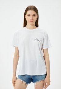 Hvid bomulds T-shirt med korte ærmer og rund halsudskæring. Har tekstprint foran i sort og rød. Sammen med denimshorts.