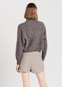 Gray, cropped knit sweater with a high neckline and loose sleeves, paired with beige tailored shorts featuring back pockets.