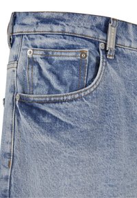 Primer plano del bolsillo de unos vaqueros de mezclilla azul claro con costuras visibles, remaches metálicos y un pasador para cinturón con una etiqueta metálica.