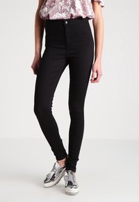 Jeans skinny negros de tiro alto, elaborados con una tela de mezcla de algodón elástica, que presentan una textura suave y un diseño clásico de cinco bolsillos.