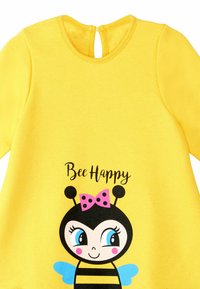 Gelbes Baumwollkleid mit einem Bienenmotiv, schwarzen Streifen, einer rosa gepunkteten Schleife und dem Text "Bee Happy". Schlüsselrochverschluss im Rücken.