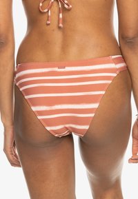 Rosa bikiniunderdel med vita horisontella ränder. Mjuk, elastisk tyg är synlig och har en liten logotyp på baksidan.