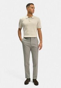 Ljusbeige ribbad polo skjorta i kombination med skräddarsydda ljusgrå byxor och mörkbruna skor. Enkel design med korta ärmar och krage.