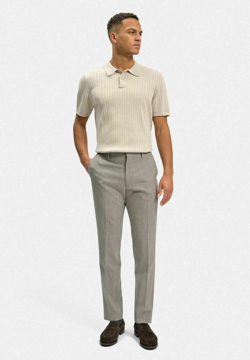 Ljusbeige ribbad polo skjorta i kombination med skräddarsydda ljusgrå byxor och mörkbruna skor. Enkel design med korta ärmar och krage.