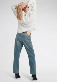 Maglione grigio chiaro a coste e jeans a gamba dritta blu scuro con etichetta in pelle sulla cintura posteriore e tacchi aperti neri.