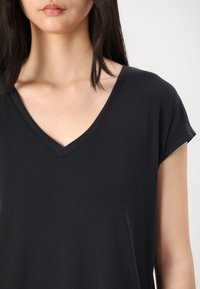 T-shirt noir à col en V avec manches courtes, texture lisse et coupe décontractée. Design simple sans motifs ni accents.