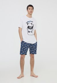 Maglietta bianca con grafica di un panda e testo "Feeling Fresh!". Pantaloni corti blu navy con motivo di panda ripetuto. Tessuto di cotone, vestibilità casual.