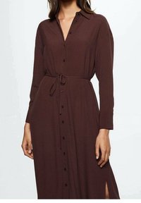 Długa, ciemno-brązowa sukienka koszulowa z miękkiego materiału, z zapięciem na guziki z przodu, wiązanym w pasie i kieszeniami po bokach.