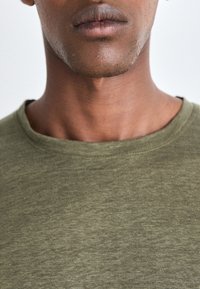 Olivegrünes Baumwoll-T-Shirt mit Rundhalsausschnitt und kurzen Ärmeln, mit einer glatten Textur und subtiler melierter Optik.