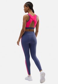 Sujetador deportivo rosa con espalda con corte, combinado con leggings azul marino que tienen rayas laterales rosas. El material parece elástico y suave.