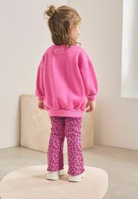 Vaaleanpunainen collegepaita ribbed-hihansuilla ja takakappaleen tarralla; vaaleanpunaiset legginsit mustalla ja oranssilla leopardikuviolla, levenevä malli ja rispaantuneet lahkeet. Valkoiset tenkat.