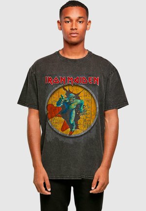 Black cotton t-shirt featuring a graphic print of a blue mummy with red accents on a yellow background, and "Iron Maiden" text at the top.