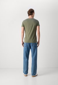 Olivenfarbene, taillierte T-Shirt mit kurzen Ärmeln, kombiniert mit hellblauen, geraden Jeans, getragen mit weißen Schuhen. Minimalistische Details und keine Muster.