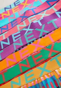 Colorful stacked fabric bands with the word "NEXT" in large, bold letters in varying colors and patterns.
