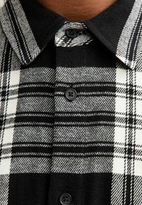 Camicia a scacchi bianca e nera con chiusura a bottoni, colletto classico, texture del tessuto morbida e bottoni neri.