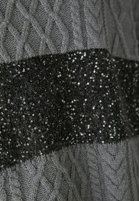 Pull en tricot gris avec un motif de torsades, orné d'une bande de sequins noirs brillants au milieu, ajoutant texture et contraste.
