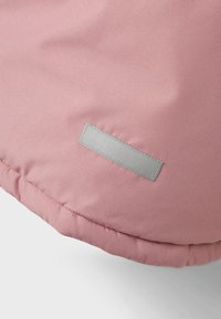 Tessuto esterno rosa con una superficie liscia e un'etichetta rettangolare argentata con testo in rilievo, attaccata in un'area d'angolo.