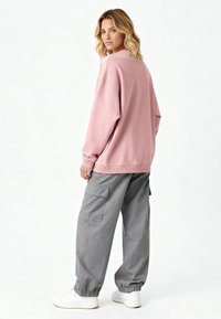 Felpa oversize rosa con polsini a coste, abbinata a pantaloni cargo grigi larghi con tasche laterali e orli elasticizzati. Sneakers bianche.