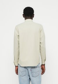 Πουκάμισο με μακριά μανίκια σε ανοιχτό πράσινο χρώμα, με γιακά και μανσέτες με κουμπιά, κατασκευασμένο από υφή υφάσματος και ευθεία πίσω ρόκα, φορεμένο με μπλε τζιν.