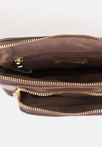 Interno di una borsa a tracolla in pelle marrone con molteplici scomparti, cerniere dorate e una superficie liscia, con un'etichetta di marca all'interno.
