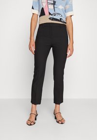 Zwarte op maat gemaakte broeken met een slim fit en een verkorte lengte. Soepele stof, zijzakken en een minimalistisch ontwerp. Gecombineerd met strappy heels.