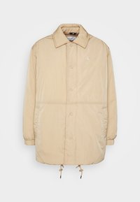 Beige pufferjack met een gladde textuur, knopenfront, oversized kraag, elastische manchetten en trekkoorden aan de onderkant. CK-logo op de borst.