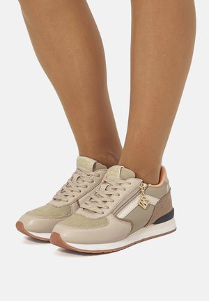 Zapatillas beige con una mezcla de materiales lisos y texturizados, que cuentan con un sistema de cordones, un cuello acolchado y un charm decorativo de cremallera.