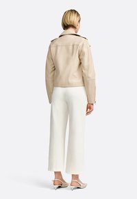 Veste de moto en cuir beige avec un col classique, des poignets zippés et un design minimaliste. Assortie à un pantalon large blanc et des chaussures légères.