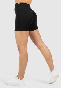 Zwarte rekbare sportshorts met een hoge tailleband, strakke pasvorm en gladde textuur, gecombineerd met witte sneakers.