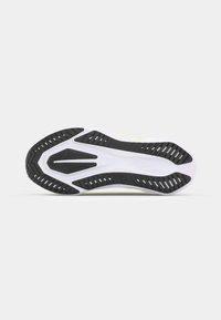 Sohle eines Sneakers mit schwarzem Gummiprofil, weißer Zwischensohle und gelben Akzenten. Entworfen mit tiefen Rillen und einer strukturierten Oberfläche.