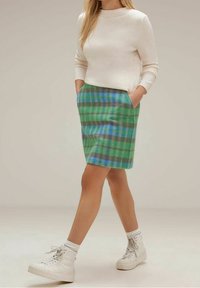 Vihreä ruudullinen hame, jossa on sinisiä ja harmaita yksityiskohtia, istuva malli ja taskut, yhdistettynä kermaiseen neuleeseen ja valkoisiin korkeakärkisiin tennareihin.