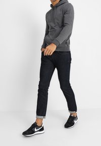 Grijze hoodie met een voorzak en een verstelbare trekkoordcapuchon, gecombineerd met slim-fit donkere spijkerbroeken en zwarte sportschoenen.