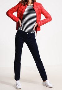 Rote wattierte Jacke, marineblaue Hose und gestreiftes Hemd mit weißen Turnschuhen. Glatte Textur, taillierte Passform und sichtbare Nähte.