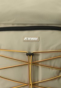 Pochette beige clair avec une fermeture éclair noire. Présente un logo K-Way et des cordons élastiques en jaune et noir, offrant des options de rangement supplémentaires.