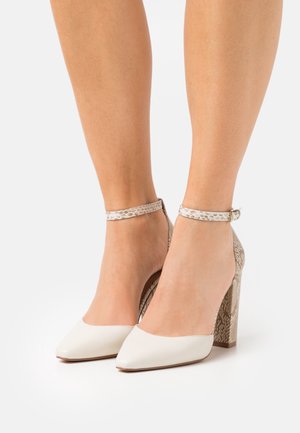 Escarpins blancs en cuir verni avec un bout pointu et une bride à la cheville, présentant un talon texturé en imprimé serpent. Surface lisse avec une finition brillante.
