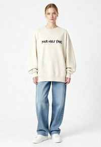 Felpa crema oversize con testo nero che recita "YOUR ONLY FANS." Abbinata a jeans di denim azzurro chiaro e sneakers bianche.