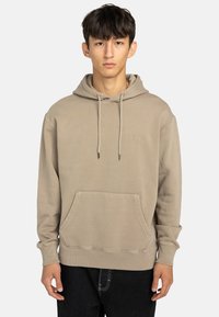 Beige huvtröja med ficka framtill. Den har dragsnören och ribbade ärmmuddar, tillverkad av en mjuk bomullsblandning.