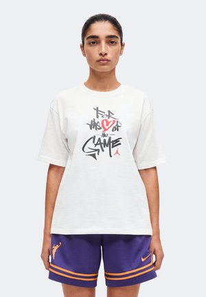 Persona che indossa una t-shirt bianca con una grafica e la scritta "For the love of the game" e pantaloncini da basket viola con strisce arancioni e loghi.