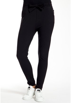 Zwarte leggings met een slim fit ontwerp, een elastische tailleband met een strikdetail, zijzakken en gecombineerd met witte sneakers.