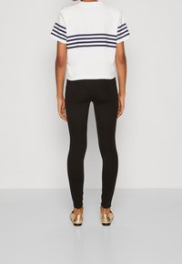 Bílý cropped top s námořnickými horizontálními pruhy na rukávech, spárovaný s černými legínami a metalickými zlatými botami. Hladká textura, ležérní střih.