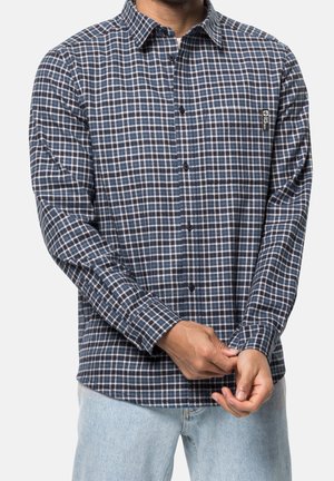 Mand iført blå og hvid ternet langærmet skjorte, der knapper manchetterne, kombineret med lyseblå jeans.